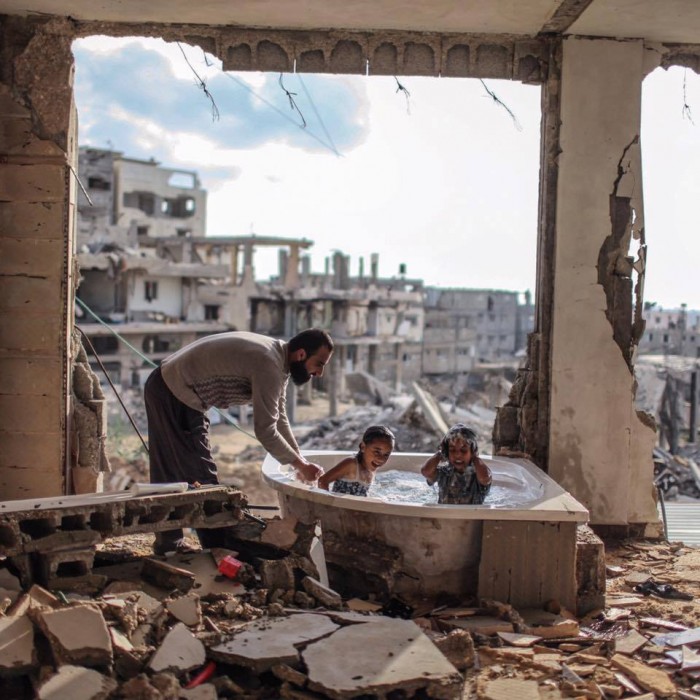 Palestinian father bathing his daughter and niece in their destroyed home